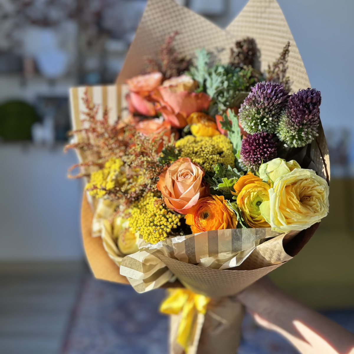 A vibrant autumn-colored bouquet wrapped in kraft paper, held in hand.