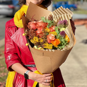 A woman in colorful attire holding a lush autumn bouquet wrapped in kraft paper, showcasing rich fall hues and textures.