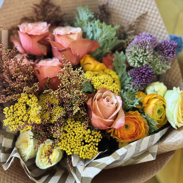 A close-up of a warm, fall-colored bouquet wrapped in rustic kraft paper.