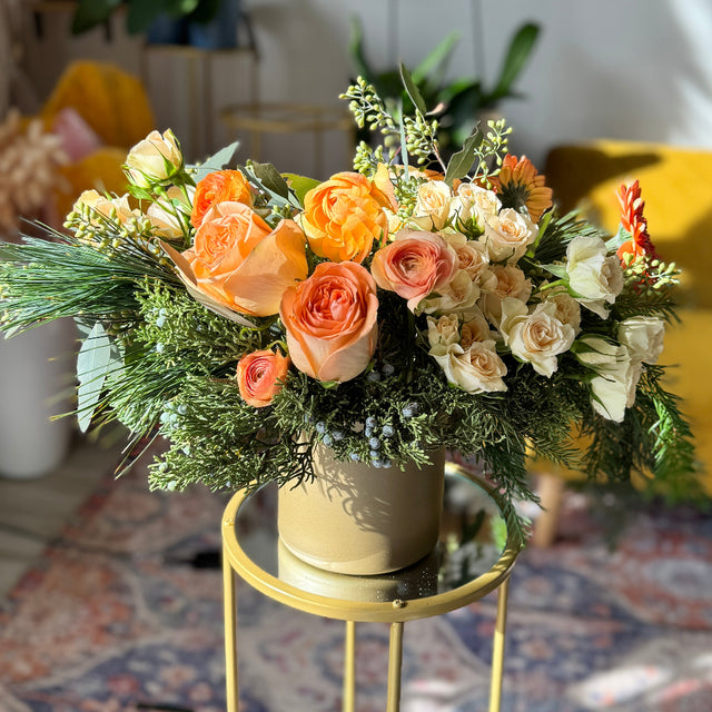 Festive table centerpiece with coral flowers, pine, juniper, and seeded eucalyptus