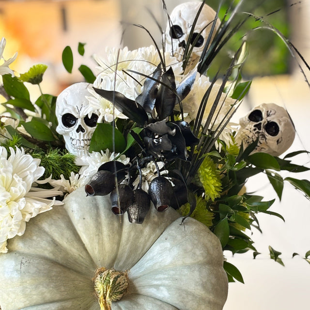 White chrysanthemums and green button mums with eucalyptus, ruscus, and miniature skulls
