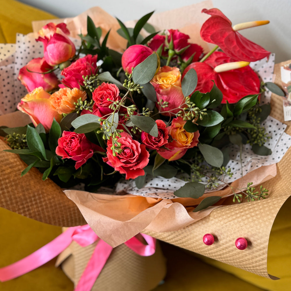 Bouquet of flowers with red roses, pink and orange flowers, and green leaves on a yellow surface.