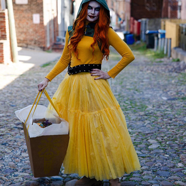 A spooky girl in costume holding a box with a bouquet of orange flowers, scary pumpkins, spiders.