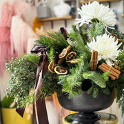 Holiday greenery and white flowers on a gold side table in a room setting.