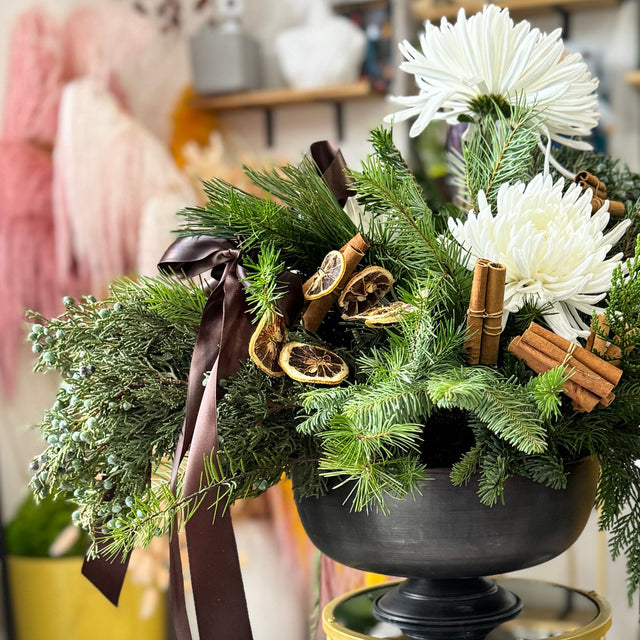 Holiday greenery and white flowers on a gold side table in a room setting.