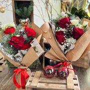 Two bouquets of red roses wrapped in brown paper with ribbons on a wooden table.