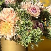 Floral arrangement in a gold vase on a reflective surface with a blurred background