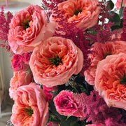 A close-up of a dense floral arrangement featuring large ruffled pink and peach roses with smaller bright pink blossoms and dark green foliage.