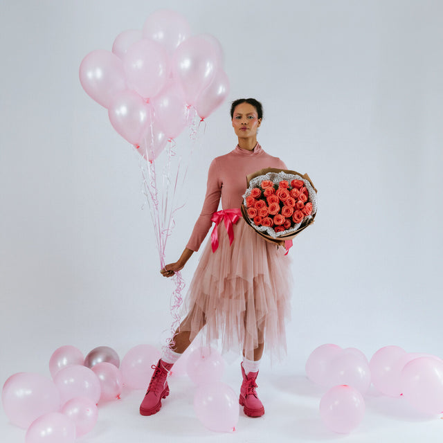 Bouquet of coral roses in the arms of a girl with pink balloons
