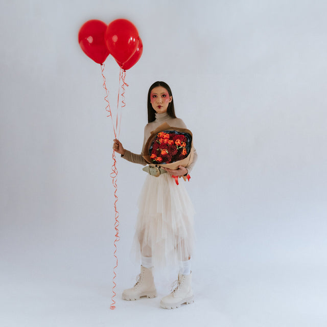Bouquet of roses, carnations, and tulips in the hands of a girl in beige with balloons