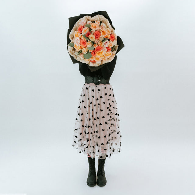 Bouquet of soft roses in black wrapping paper in the hands of a girl