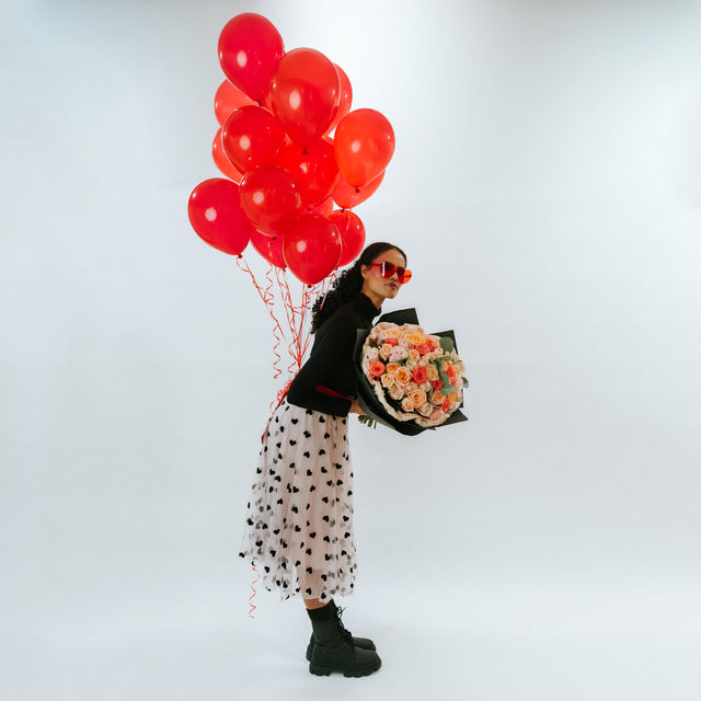 Buquet of light pink roses, coral roses, and white roses in black wrapping paper in the hands of a girl with balloons