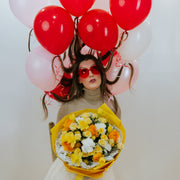 Bouquet of yellow and white flowers in the arms of a girl with balloons