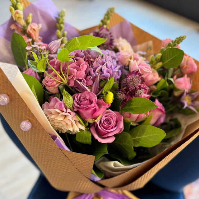 bouquet featuring lavender hydrangea, lavender roses, soft pink spray roses, clematis, and snapdragons.