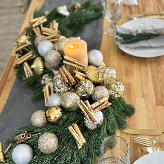 Luxury holiday centerpiece with fresh pine, gold ornaments, matte silver accents, and decorative cinnamon sticks
