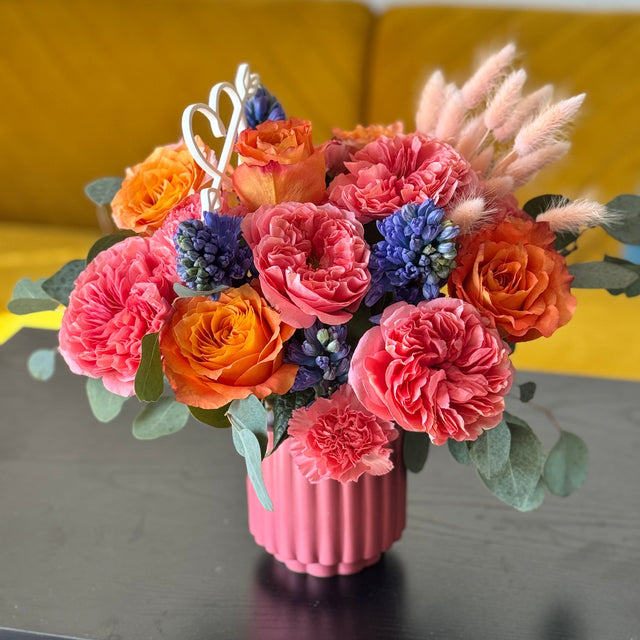 Pink and coral rose arrangement with blue hyacinth in a ribbed pink vase
