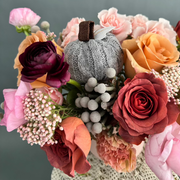 Blend of terracotta and pink flowers with a gray knitted pumpkin, in a pink clay vase.