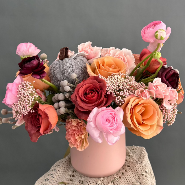 Pink Whisper Centerpiece in a pink clay vase, soft pink and orange flowers and a gray knitted pumpkin