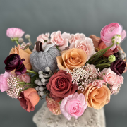 Pink ranunculus, roses, and silver brunia with a gray knitted pumpkin.