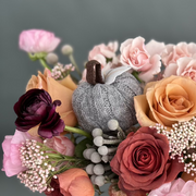 Pink ranunculus, roses, and silver brunia with a gray knitted pumpkin.