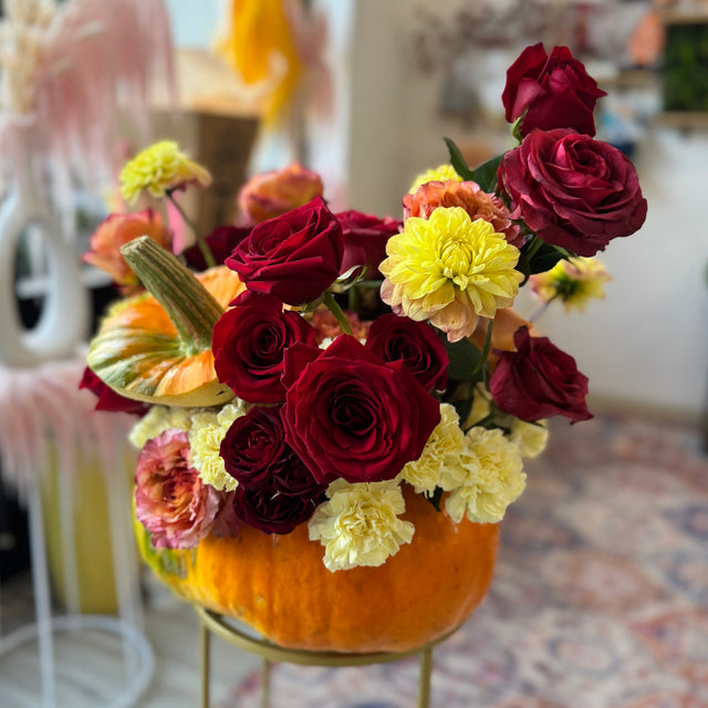 pumpkin flower arrangement with dahlias, roses, and mums in warm fall colors.