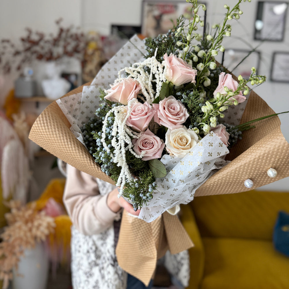 Romantic winter bouquet featuring pink roses, white florals, and cascading amaranthus in kraft and gold tissue wrapping.