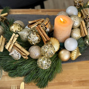 S-shaped holiday centerpiece made of fresh pine with gold and matte silver ornaments and space for a candle