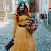 A spooky girl in costume holding a bouquet of orange flowers with scary pumpkins, spiders in one hand and a butcher knife in another.