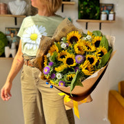 Top view of a bouquet held by a florist, showcasing the full arrangement of sunflowers and asters.