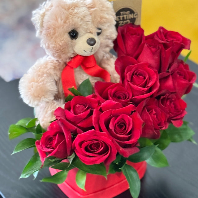 Teddy bear with red roses in a heart-shaped vase on a dark surface