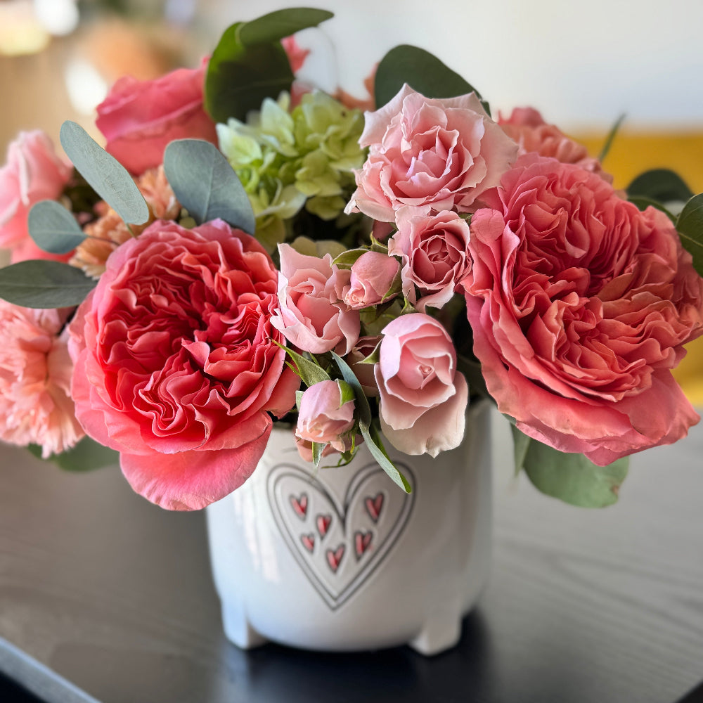 Love Notes Valentine’s arrangement with pink roses and blue hydrangea in a white heart vase