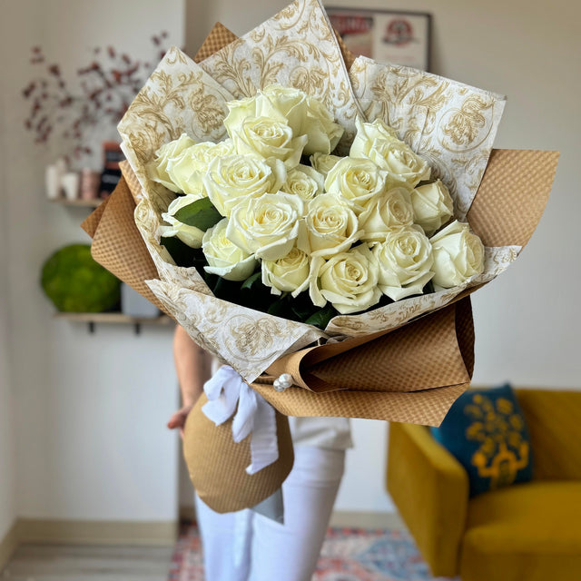 Elegant bouquet of white roses wrapped in eco-friendly kraft paper with a white ribbon and bead details.