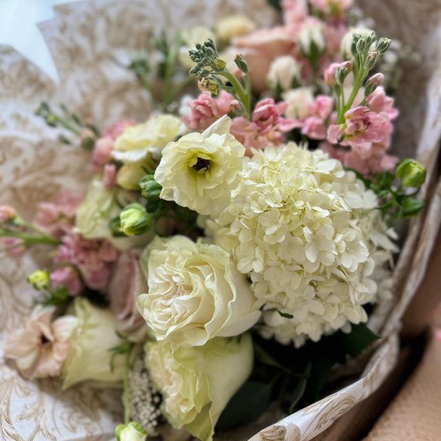 Close-up of an elegant fresh cut flowers bouquet with white hydrangeas, white roses, ranunculus, and light pink stock flowers.