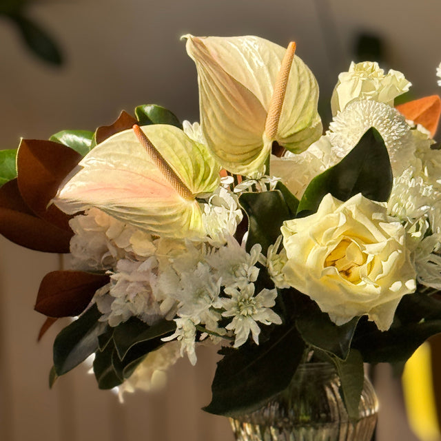 Close-up of Winter Grace arrangement showing white anthuriums, roses, and hydrangeas surrounded by magnolia leaves.