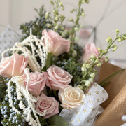 Eco-wrapped bouquet of pink roses and white flowers with winter greenery and flowing amaranthus.