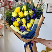  Graduation bouquet featuring yellow roses, blue delphinium, and palm leaves