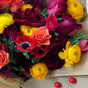 Close-up of the Juicy Fall bouquet, highlighting vibrant yellow ranunculuses, red roses, orange spray roses, and red anemones.