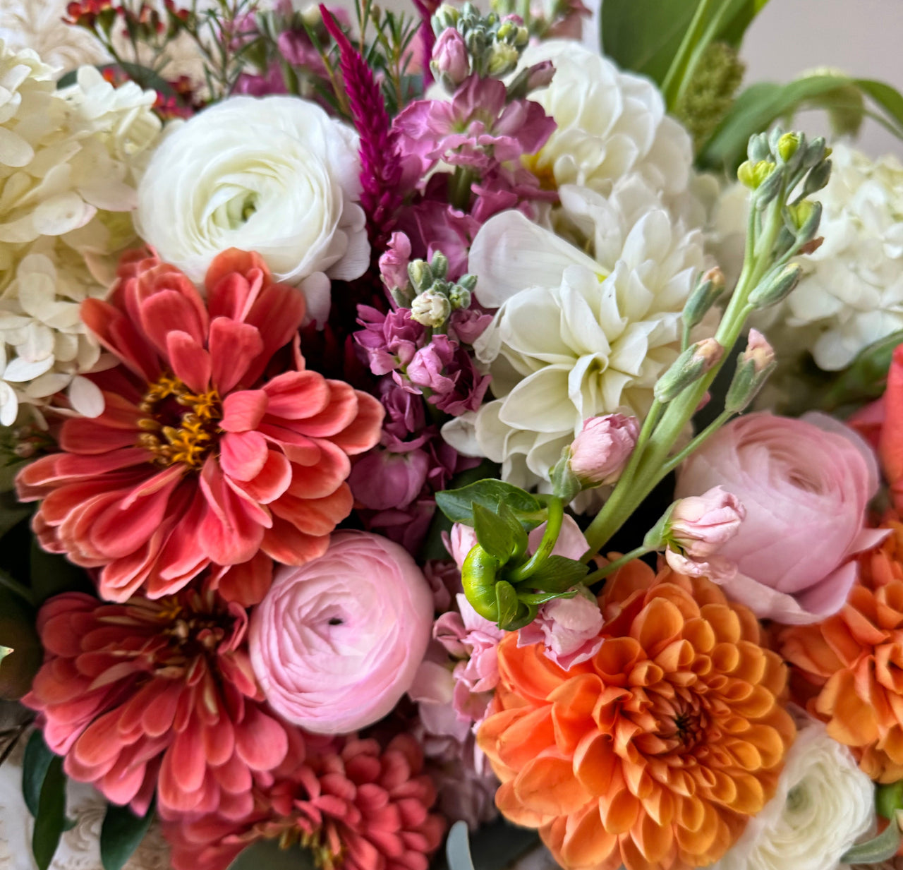 Close-up of the Bouquet showcasing vibrant orange, pink and white flowers, including dahlias, carnations, and roses, with accents of eucalyptus and hydrangeas.