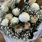 Magnolia Mist all-white bouquet by Flowers’ Cuddles in Springfield, VA — mums, roses, magnolia leaves, and baby’s breath in kraft wrapping.