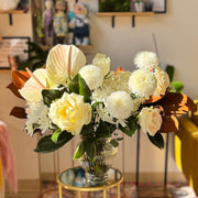 Winter Grace arrangement featuring white roses, hydrangeas, mums, and anthuriums with glossy magnolia leaves in a modern vase.