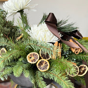 Decorative floral arrangement with greenery, white flowers, and citrus slices in a pot.
