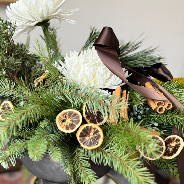 Decorative floral arrangement with greenery, white flowers, and citrus slices in a pot.