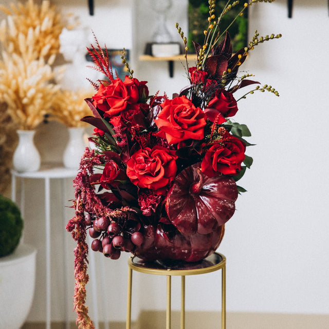 Modern autumn floral arrangement featuring vibrant red flowers in a beautifully painted pumpkin.