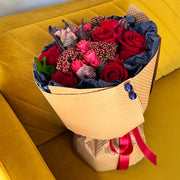 Handcrafted Rustic Flame bouquet with glowing red roses, parrot tulips, soft spray roses, and warm brown ruscus in stylish navy and kraft wrapping.