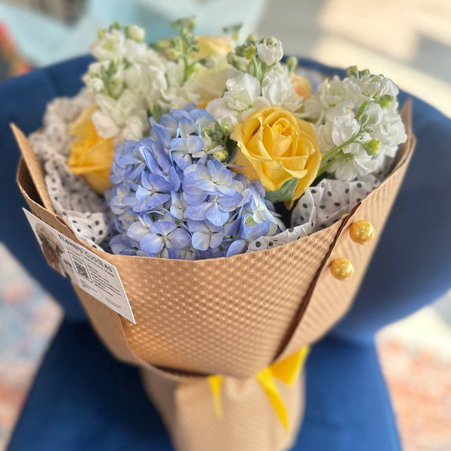 bouquet with yellow roses, blue hydrangea, and white stock in eco-friendly wrapping