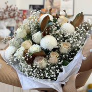 bouquet with white mums, roses, baby’s breath, and magnolia leaves wrapped in kraft paper.