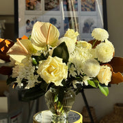 Bouquet of flowers in a clear vase on a small round table with 'Flowers Cuddles' poster in the background.