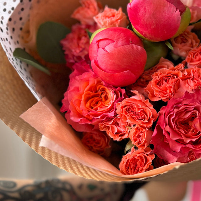 Close-up of coral peonies, roses, and spray roses showing delicate petals and rich texture.