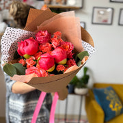 Bouquet of pink and orange flowers in a brown paper wrap held by a person in a living room.
