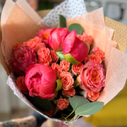 Bouquet of pink and orange flowers wrapped in brown paper held by a person.
